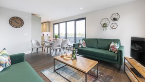 Een moderne woonkamer met een groene bank, een houten salontafel en een eethoek met stoelen en een tafel.