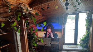 Ett mysigt rum med ett träpanelat tak, en tv, en krukväxt och ett fönster med utsikt över omgivningen.