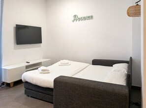 Une chambre à coucher moderne, équipée d’un lit, d’une télévision, d’une table de chevet et d’un panneau décoratif fixé au mur.