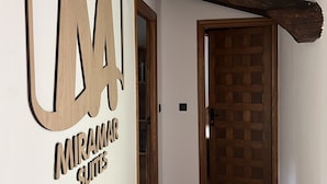 Un couloir avec un plafond en bois et une porte donnant sur une pièce. Une pancarte sur le mur indique : « Miramar Suites ».