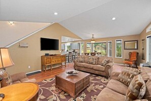 A spacious living room with a high ceiling, a large flat-screen TV, a wooden coffee table, and a sofa set. - 3BR Retreat | Hot Tub, Pool Table & Foosball | Near Golf & Leavenworth (Leavenworth)