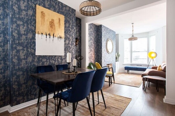 A dining area with a dark wooden table, blue chairs, and a large abstract painting on the wall.