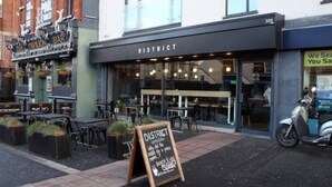 Un restaurante llamado 'District' con terraza y un letrero en la fachada.