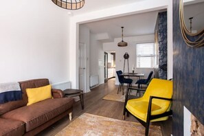 A modern living room with a brown sofa, yellow armchair, and a dining area with a table and chairs.