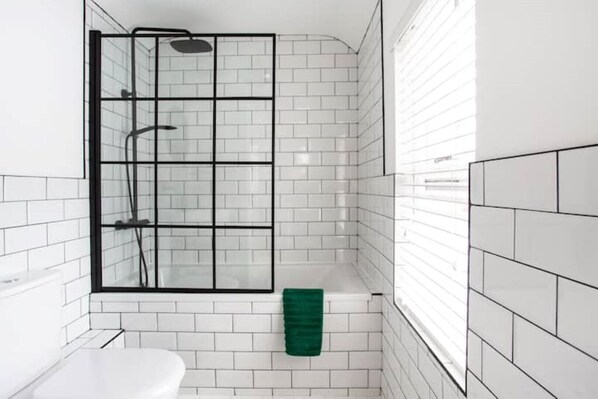 A modern bathroom with white subway tiles, a glass shower enclosure, a green bath mat, and a white sink. - Luxurious 4-Bed Townhouse in the Heart of Belfast (Belfast)