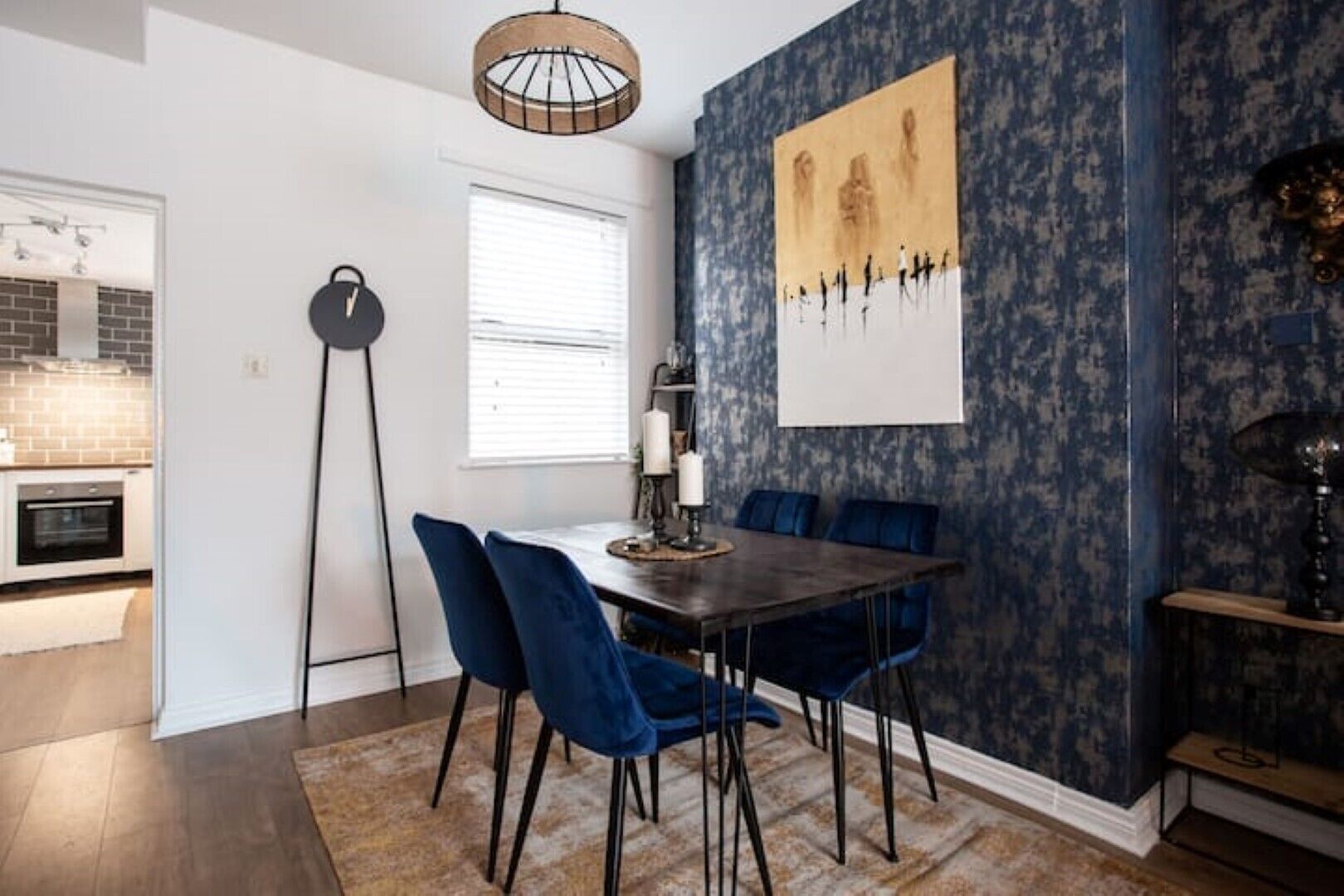 A dining area with a dark wooden table, blue velvet chairs, and a patterned wallpaper.