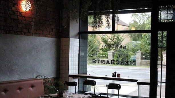 Un restaurante con paredes de ladrillo, un amplio ventanal con vistas a la calle y áreas verdes, y un espacio con bancos.