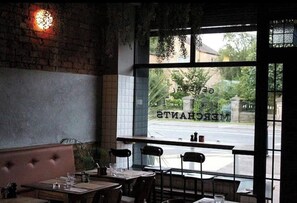 An interior view of a restaurant with brick walls, a large window with a view of a street, and a seating area with tables and chairs. - Luxurious 4-Bed Townhouse in the Heart of Belfast (Belfast)
