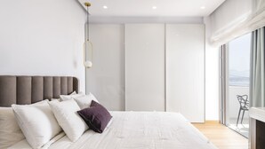A modern bedroom with a large bed, a headboard, and a view of the outdoors through a large window.