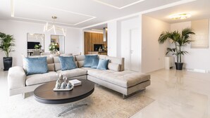 A modern living room with a sectional sofa, a round coffee table, and a dining area in the background.