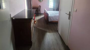 Un pasillo estrecho con una cama, una mesita y un espejo en la pared.