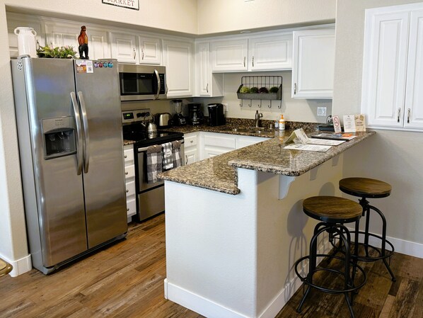 A modern kitchen with white cabinetry, stainless steel appliances, a granite countertop, and a bar stool.