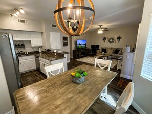 A modern kitchen with white cabinets, a granite countertop, and a wooden dining table with a fruit centerpiece.