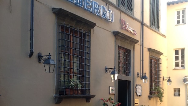 A building with the sign "ALBERGO" and "Hotel Alberghetti" indicating it is a hotel. There are potted plants on the ground floor and a street in front. - Diana (Lucca)