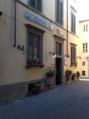 A building with the sign "ALBERGO" and "Hotel Alberghetti" indicating it is a hotel. There are potted plants on the ground floor and a street in front.