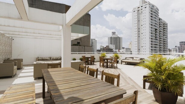An outdoor terrace with a long wooden table and chairs, surrounded by potted plants and a city skyline view. - Av0203 Studio Avanhandava (São Paulo)
