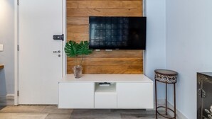 A modern living room with a wooden accent wall, a flat-screen TV mounted above a white entertainment unit, and a small side table. - Av0203 Studio Avanhandava (São Paulo)