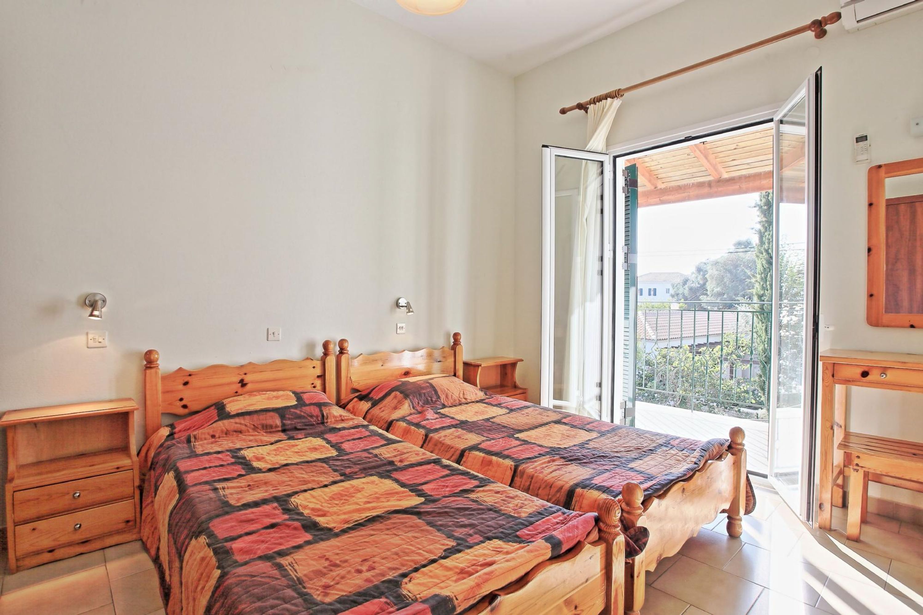 A bedroom with two wooden beds, a wooden nightstand, a wooden dresser, and a large sliding glass door leading to a balcony.