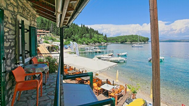 Una terraza con asientos al aire libre con vista a un lago tranquilo, rodeada de árboles y barcos.