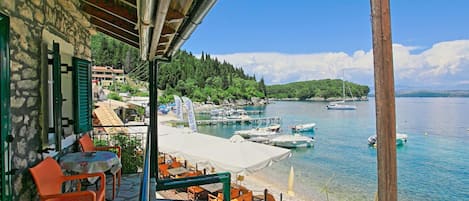 A terrace with outdoor seating overlooking a calm lake, surrounded by trees and boats.