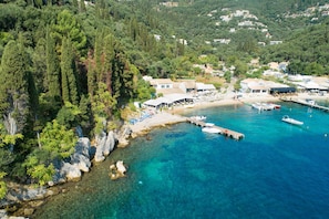 A coastal area with clear turquoise waters, a dock with boats, and a small beach with umbrellas.