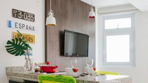 Ett modernt kök med en bänkskiva i granit, gula och gröna stolar, en tv som är monterad på väggen och ett fönster som släpper in naturligt ljus.