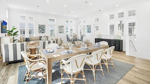 A spacious dining area with a wooden table and wicker chairs, surrounded by white walls and large windows.
