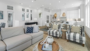 A spacious living room with a sofa, armchairs, and a coffee table. There is a dining area with chairs and a kitchen in the background.