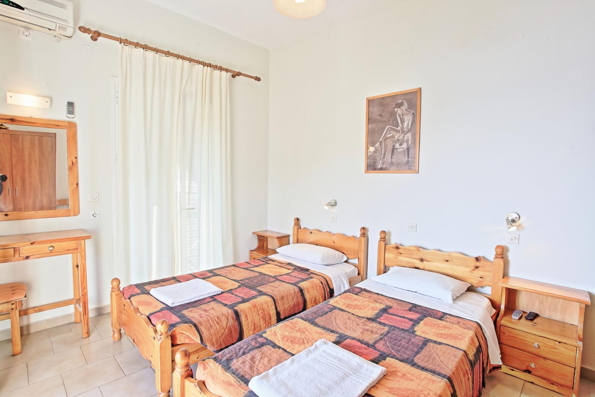 Ein Schlafzimmer mit zwei Holzbetten, einem Schreibtisch aus Holz, einem Spiegel, einem Gemälde und einem Nachttisch mit Lampe.