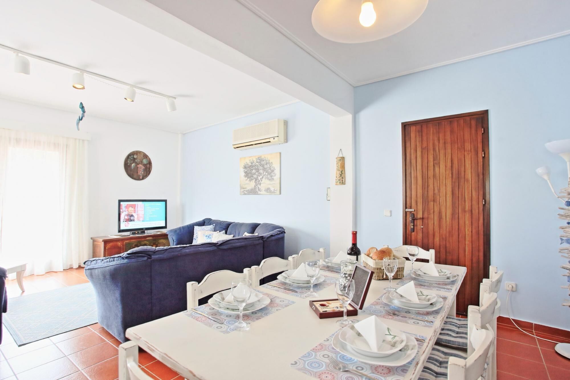 Un coin repas avec une table dressée pour quatre personnes, un canapé en arrière-plan et une porte en bois.