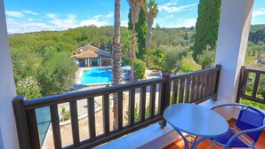 Un balcon donnant sur une piscine, une maison et la végétation environnante.