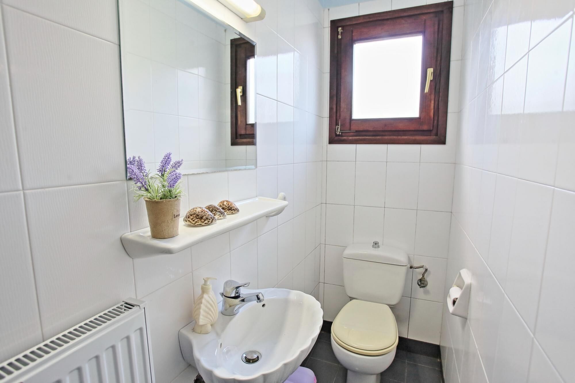 A small bathroom with a toilet, sink, and a window above the toilet.