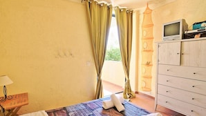 A hotel room with a bed, a TV on a wooden cabinet, and a balcony with curtains. - Casa do Tina in Mparmpati (Corfu)
