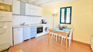 A compact kitchen with white cabinets, a washing machine, and a dining area with a table and chairs. - Casa do Tina in Mparmpati (Corfu)