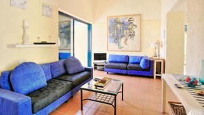 A living room with two blue sofas, a glass coffee table, a painting on the wall, and a TV on a stand. - Casa do Tina in Mparmpati (Corfu)