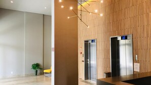 A modern lobby with two elevators, a reception desk, and a potted plant.