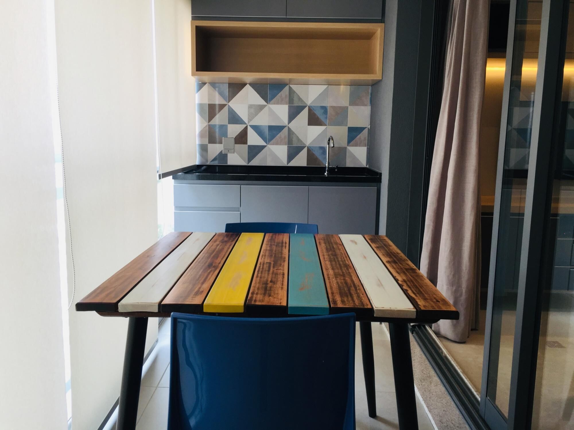 Une cuisine compacte au design moderne, dotée d’un crédence aux motifs géométriques et d’une table en bois aux rayures colorées.