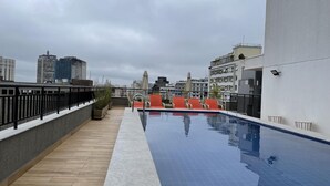 A rooftop pool with a view of city buildings, a wooden deck, and outdoor seating. - Ycp1903 in S o Paulo (São Paulo)