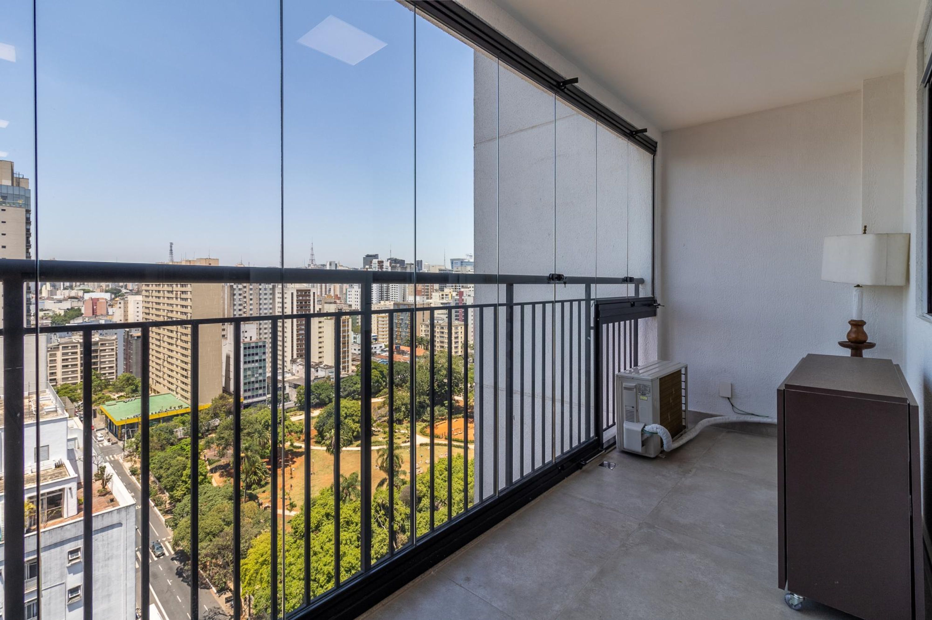 A balcony with a city view, a small air conditioning unit, and a lamp.