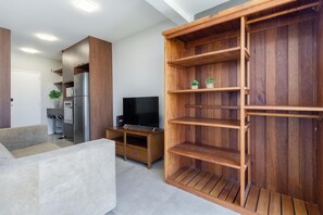 Uma sala moderna com um armário de entretenimento em madeira, uma TV de tela plana e uma área de refeições com geladeira.