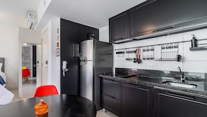 A modern kitchen with black cabinets, a stainless steel refrigerator, and a black countertop. There is a dining table with a red chair and a yellow chair. - Av0606 Studio Avanhandava (São Paulo)