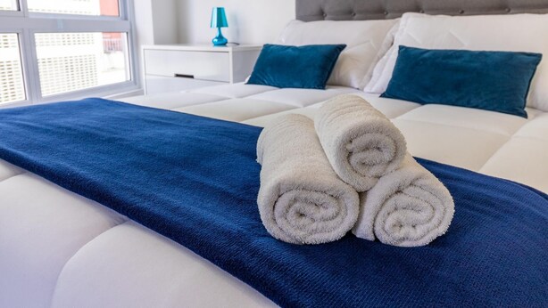 A neatly made bed with blue and white bedding, two rolled towels, and a nightstand with a lamp. - Av0606 Studio Avanhandava (São Paulo)