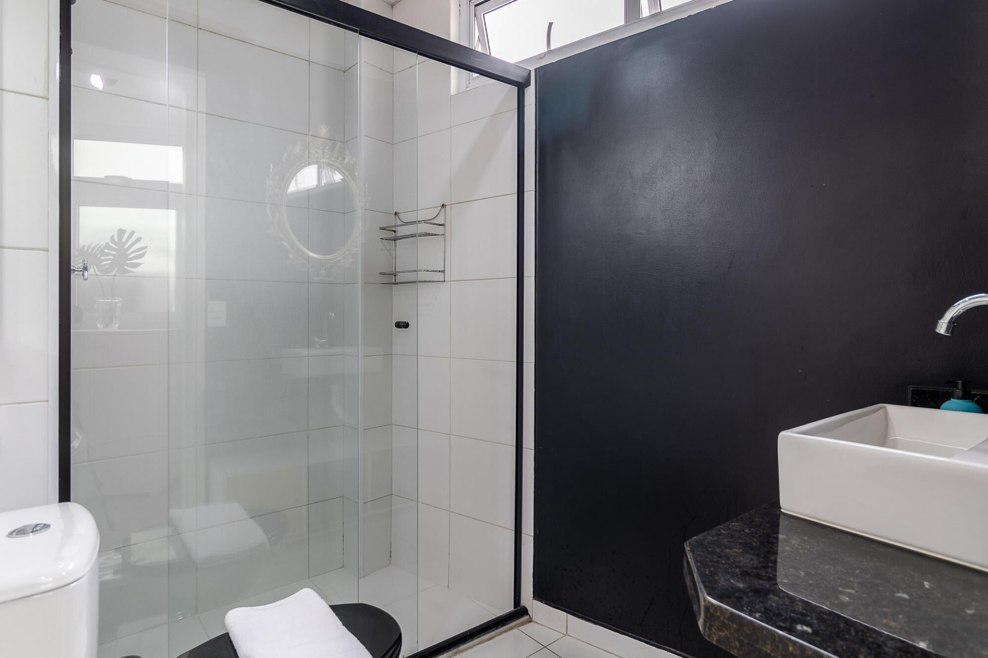 A modern bathroom with a glass shower enclosure, a black accent wall, and a white sink with a black countertop.