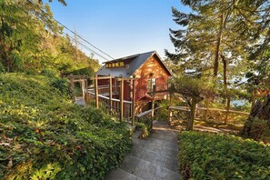 A cabin with a metal roof, surrounded by dense greenery and a wooden deck.