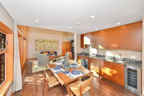 A modern kitchen with wooden cabinets, a dining area with a table set for four, and a large window providing natural light.