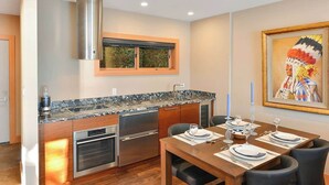 Eine moderne Küche mit Backofen, Edelstahl-Dunstabzugshaube und einer Arbeitsplatte aus Granit. Ein Esstisch ist gedeckt mit Tellern, Gläsern und einer Tischdekoration.