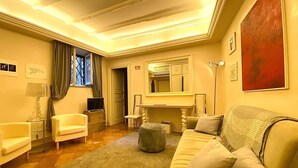 Un salon comprenant un canapé, des fauteuils, une table basse, un téléviseur, une lampe et un grand tableau accroché au mur.