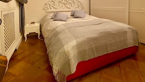 Une chambre à coucher avec un lit blanc, un piédestal rouge, une table de chevet blanche et une armoire blanche.