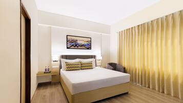 A hotel room with a bed, bedside tables, a painting, and a curtain.