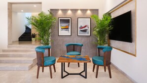A modern living room with a wooden coffee table, two wicker chairs with blue cushions, a flat-screen TV mounted on the wall, and framed artwork depicting boats. - Keys Lite Sreekanya Visakhapatnam (Visakhapatnam)